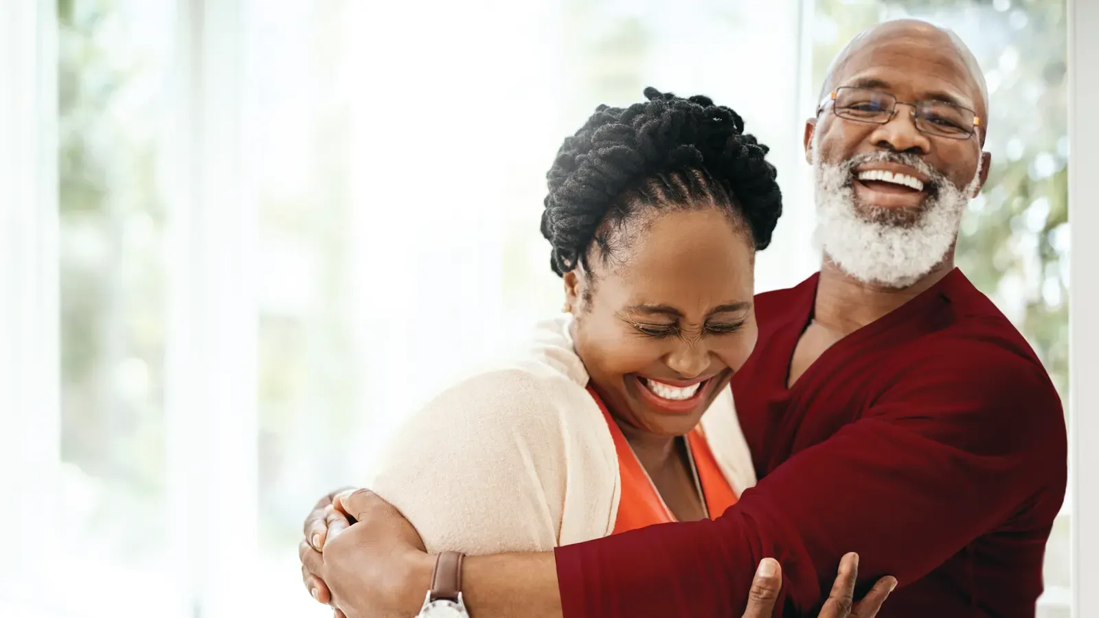 A caregiver and an older man laughing together with his arm around her shoulder